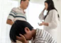 Asian boy kid sitting and crying on bed while parents having fighting or quarrel conflict at home. Child covering face and eyes with hands do not want to see the violence. Domestic problem in family.