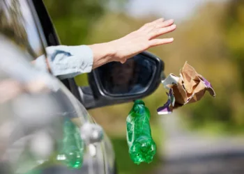 Close Up Of Driver In Car Dropping Trash Out Of Window On Country Road