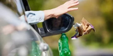 Close Up Of Driver In Car Dropping Trash Out Of Window On Country Road