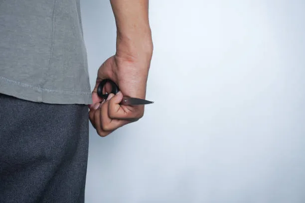 a person's hand is holding a pair of scissors, the concept of being defensive or threatening. photo illustration of murder, robbery.