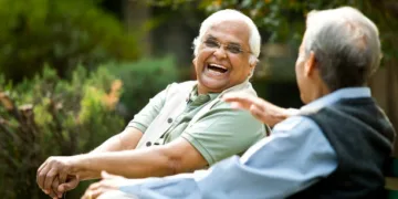 Two retired elderly men sitting on a park bench and having fun