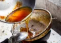 Pouring used cooking oil from frying pan into colander.