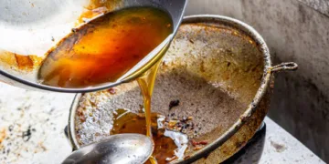 Pouring used cooking oil from frying pan into colander.