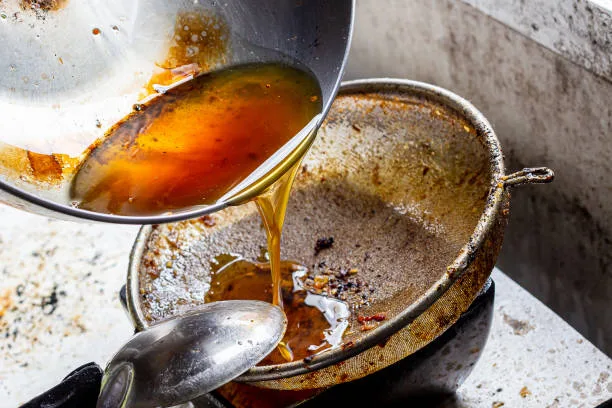 Pouring used cooking oil from frying pan into colander.