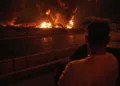 A man looks at flames rising from an oil storage facility after it appeared to have been struck by an Israeli strike in Tehran, Iran, early Sunday, June 15, 2025. (AP Photo/Vahid Salemi)