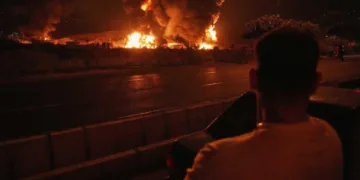 A man looks at flames rising from an oil storage facility after it appeared to have been struck by an Israeli strike in Tehran, Iran, early Sunday, June 15, 2025. (AP Photo/Vahid Salemi)