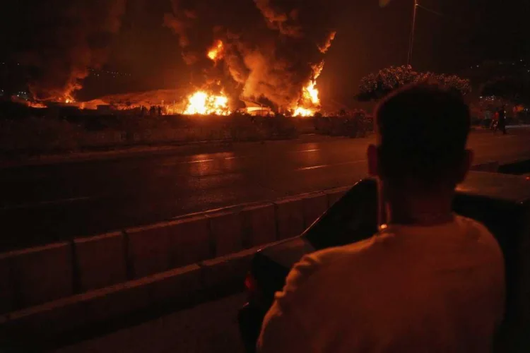 A man looks at flames rising from an oil storage facility after it appeared to have been struck by an Israeli strike in Tehran, Iran, early Sunday, June 15, 2025. (AP Photo/Vahid Salemi)