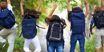 Rear-view of five children jumping in the air wearing backpacks