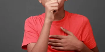 Boy coughs by closing his mouth by hands