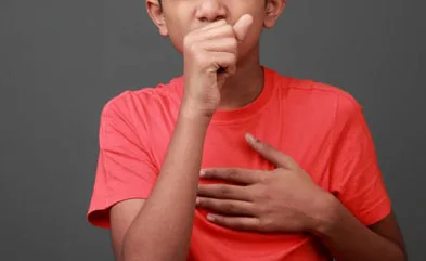Boy coughs by closing his mouth by hands